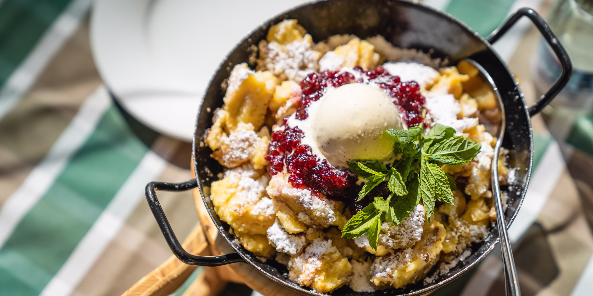 Frisch servierter Kaiserschmarrn mit Staubzucker, Beerenkompott, einer Kugel Vanilleeis und Minze.