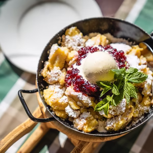 Frisch servierter Kaiserschmarrn mit Staubzucker, Beerenkompott, einer Kugel Vanilleeis und Minze.