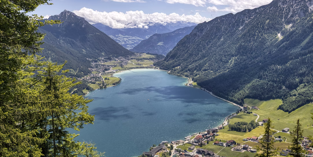 Weitläufiger Sommerblick auf den türkisblauen Achensee, die umliegenden Orte und die bewaldeten Bergflanken.