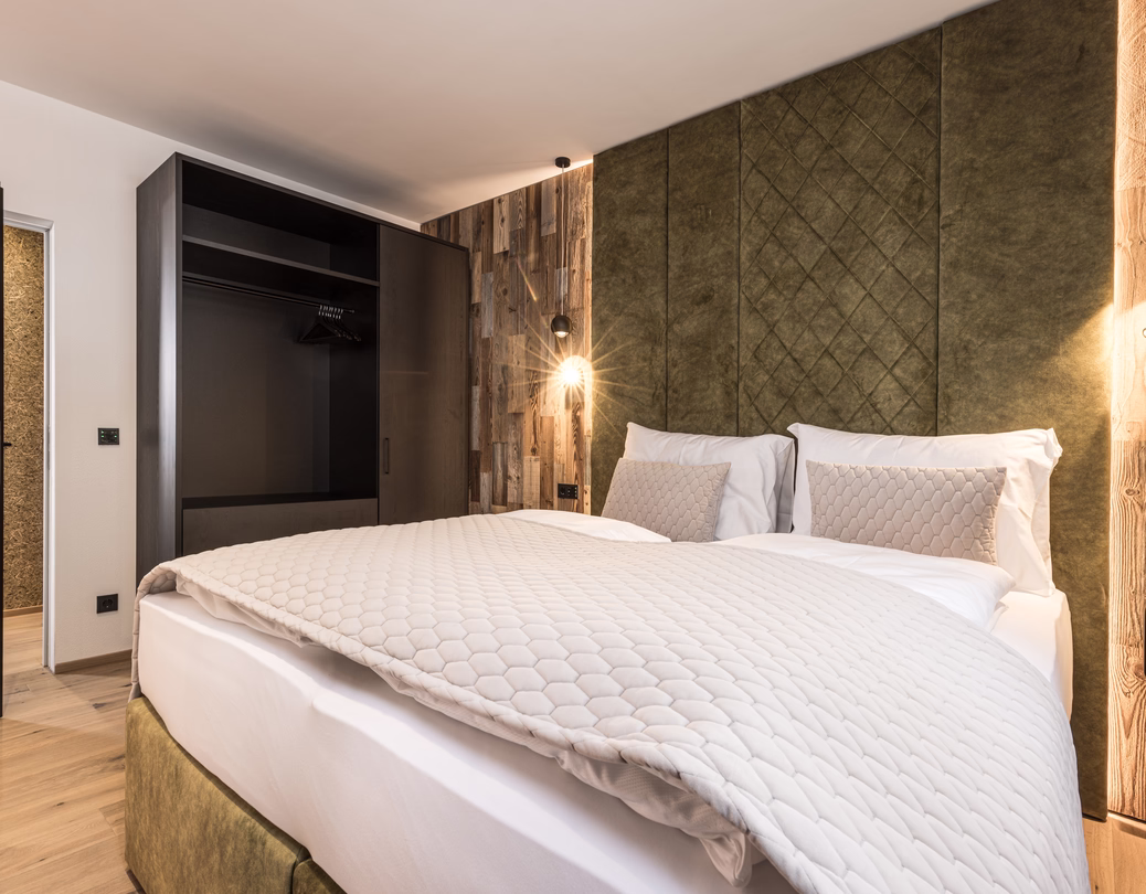 Modernes Schlafzimmer mit großem Doppelbett, grünem gepolstertem Kopfteil, rustikalen Holzelementen und offenem Kleiderschrank.