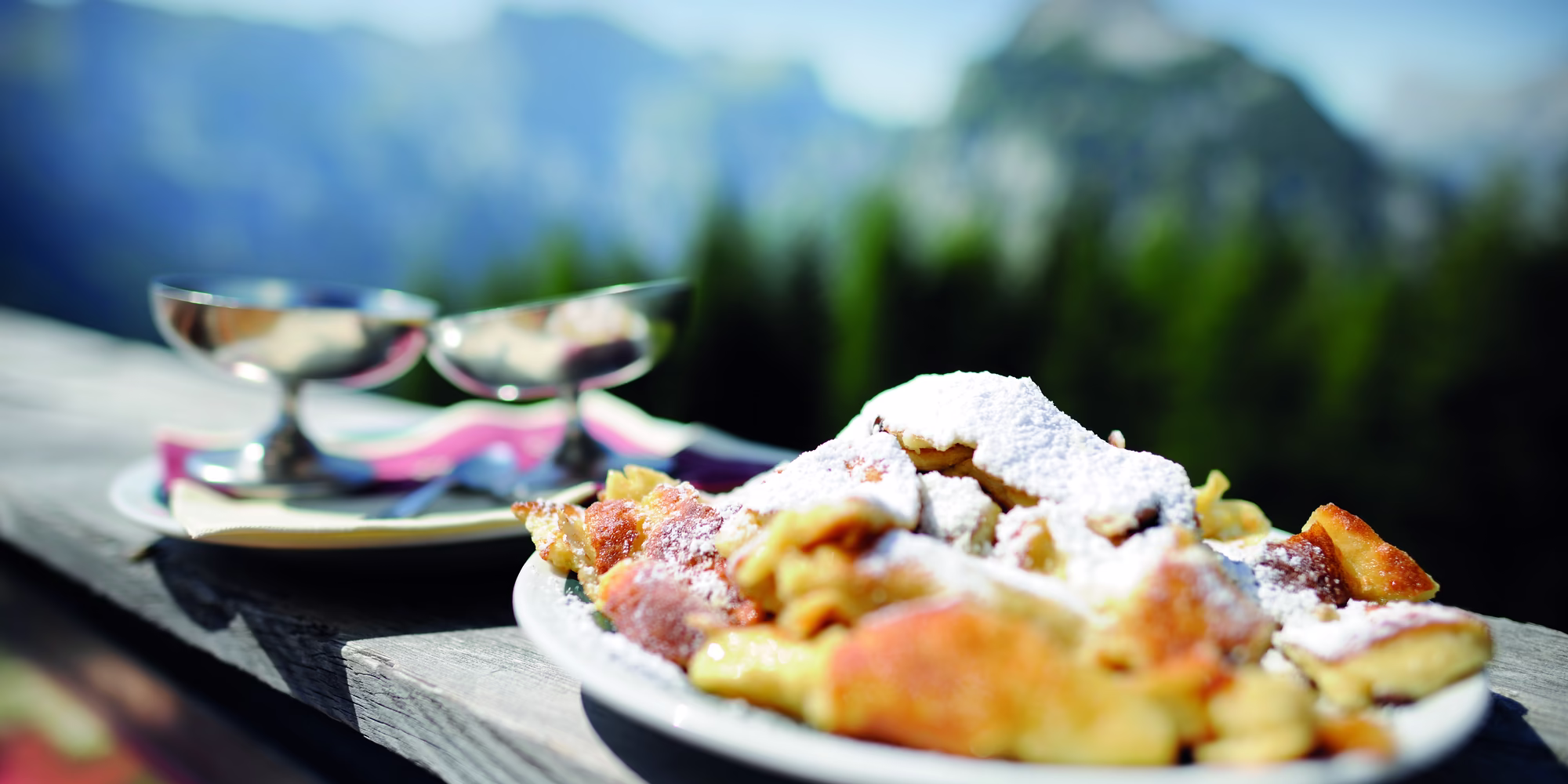 Frisch servierter Kaiserschmarrn mit Staubzucker auf einer sonnigen Terrasse mit Blick auf die Bergwelt am Achensee.
