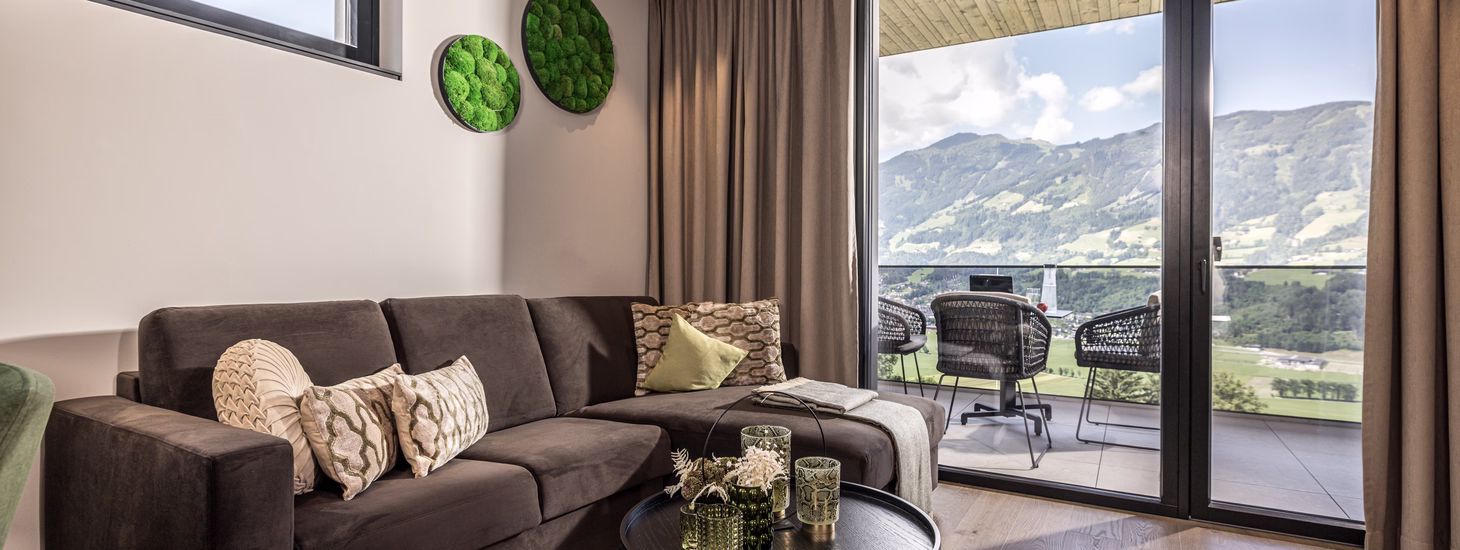 Gemütliche Sitzecke der Panorama Eagle Lodge mit Sofa, rundem Couchtisch und direktem Zugang zum Balkon mit Bergblick.