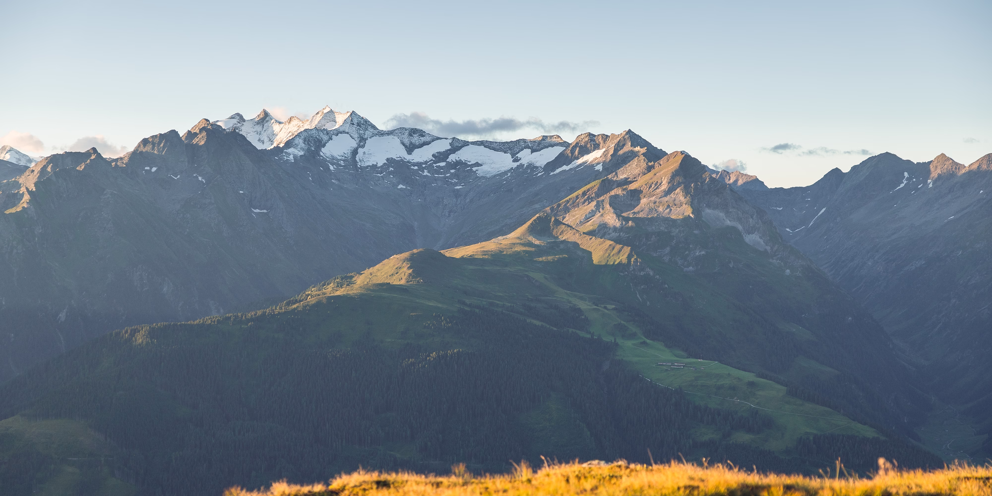 Weites Bergpanorama bei Gerlos mit sonnenbeschienenen Almwiesen, bewaldeten Hängen und schneebedeckten Gipfeln.
