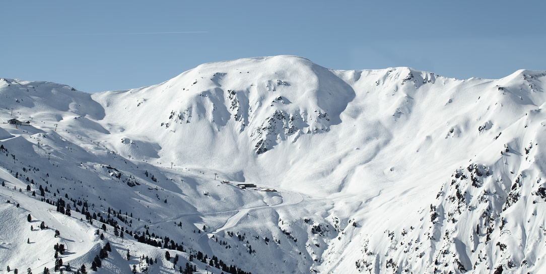 Weites Winterpanorama mit tief verschneiten Hängen, Felsformationen und einzelnen Bäumen im Skigebiet Hochfügen.