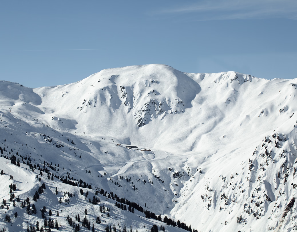 Weites Winterpanorama mit tief verschneiten Hängen, Felsformationen und einzelnen Bäumen im Skigebiet Hochfügen.