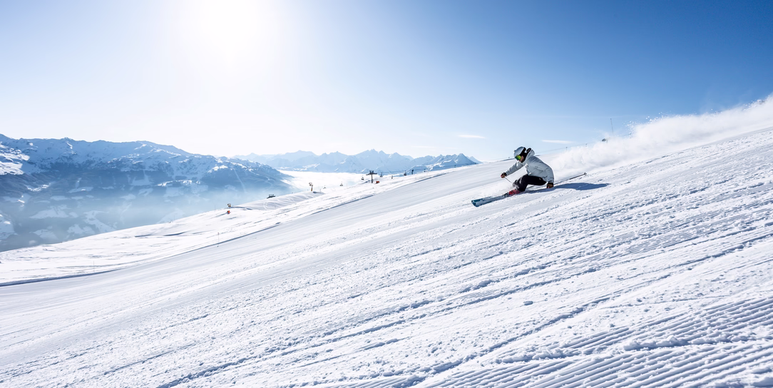 Skifahrer zieht bei strahlendem Sonnenschein eine dynamische Kurve auf einer breiten Piste im Skigebiet Hochzillertal.