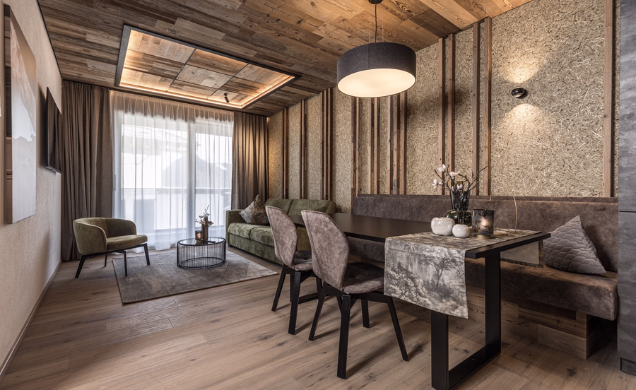 Warmer Wohn- und Essbereich mit gepolsterter Sitzbank, grünem Sofa, Holzelementen und naturbelassener Wandgestaltung.