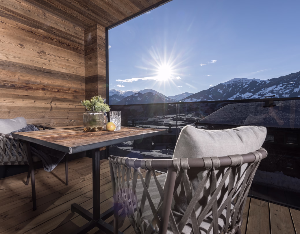 Überdachter Holzbalkon mit Tisch und bequemen Sitzplätzen sowie sonnigem Ausblick auf die verschneite Zillertaler Bergwelt.
