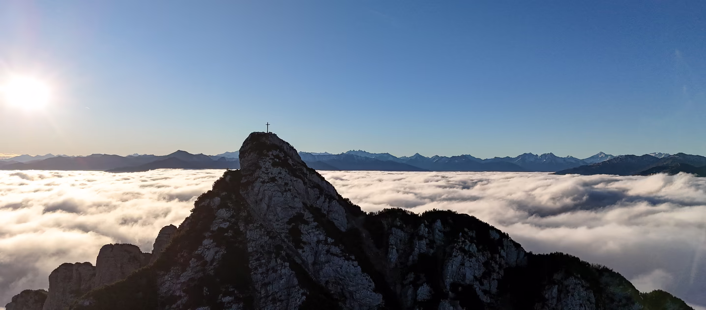 Felsiger Gipfel des Ebner Jochs mit Gipfelkreuz über einem dichten Wolkenmeer im klaren Herbstlicht.