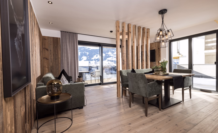 Heller offener Wohn- und Essbereich im Apartment 7 Reasons mit großen Fensterflächen, Balkonzugang und Blick in die Winterlandschaft.