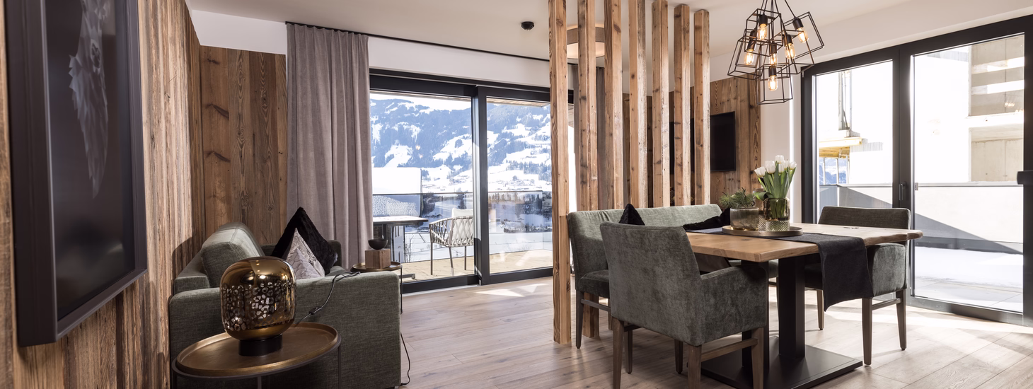 Heller offener Wohn- und Essbereich im Apartment 7 Reasons mit großen Fensterflächen, Balkonzugang und Blick in die Winterlandschaft.