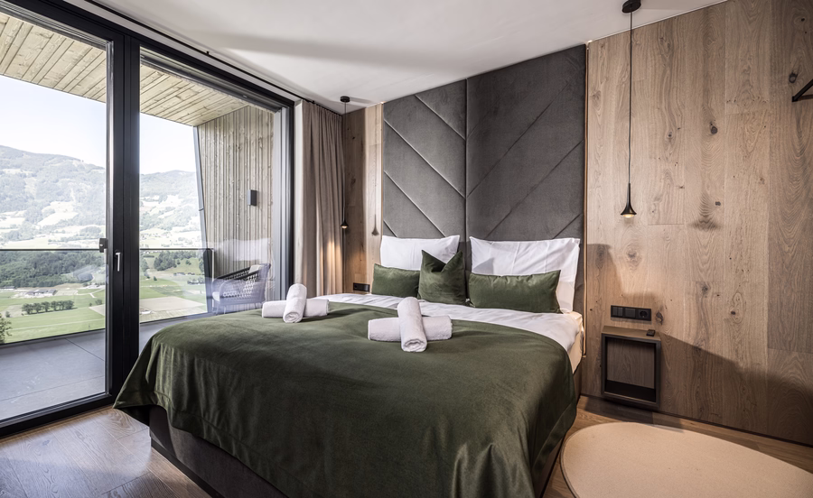Das stilvolle Schlafzimmer der Panorama Nature Lodge bietet ein Doppelbett mit grünen Akzenten und direkten Zugang zum Balkon mit Bergblick.