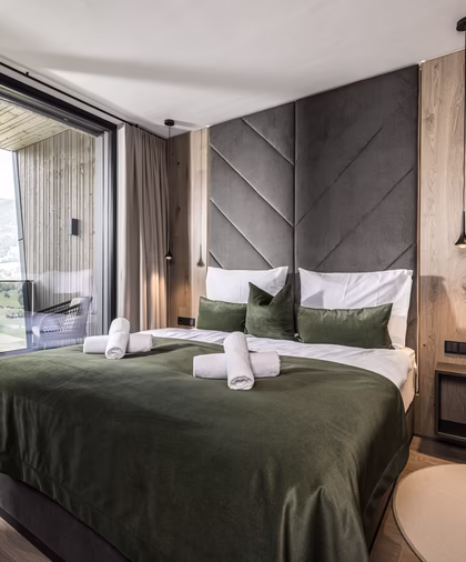 Das stilvolle Schlafzimmer der Panorama Nature Lodge bietet ein Doppelbett mit grünen Akzenten und direkten Zugang zum Balkon mit Bergblick.