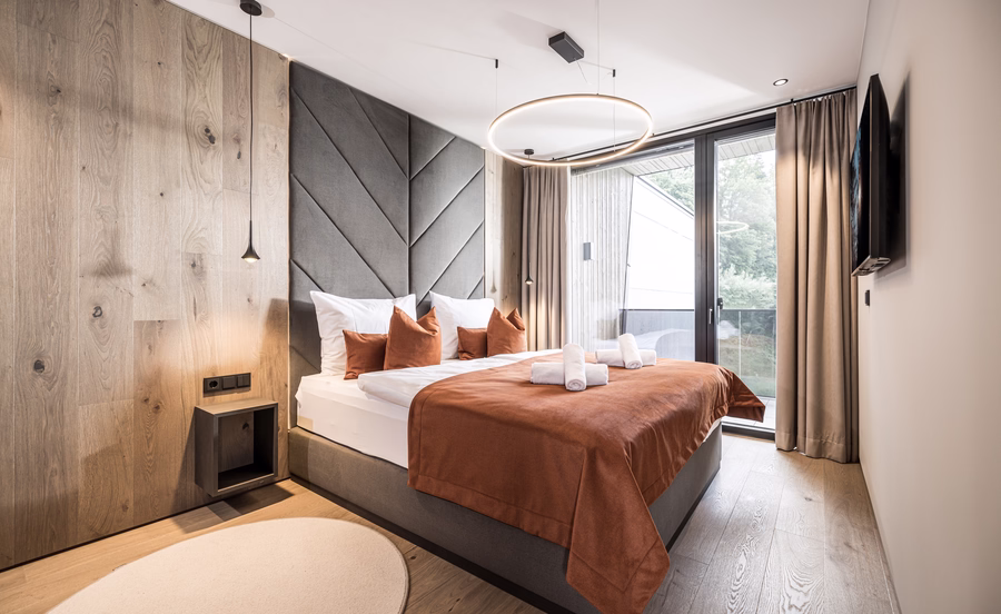 Das moderne Schlafzimmer der Panorama Nature Lodge verbindet ein gemütliches Doppelbett, warme Holzelemente und einen direkten Zugang zum Balkon.