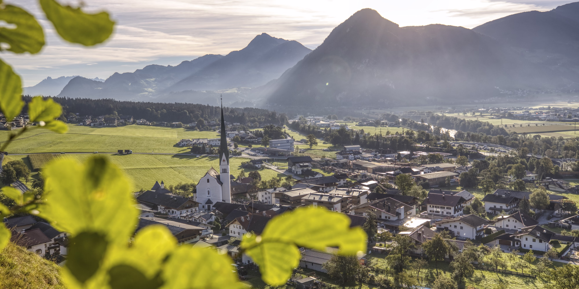 Sonniger Panoramablick auf Wiesing mit Kirche, grünen Wiesen und der markanten Bergkulisse rund um den Achensee.