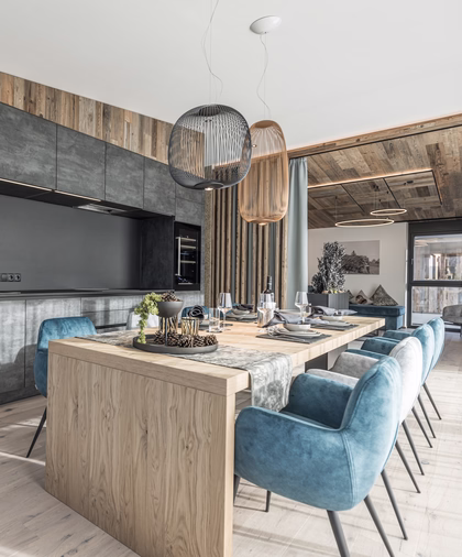 Großzügiger Essbereich im Penthouse mit langem Holztisch, blauen Polsterstühlen und moderner offener Küchenzeile.
