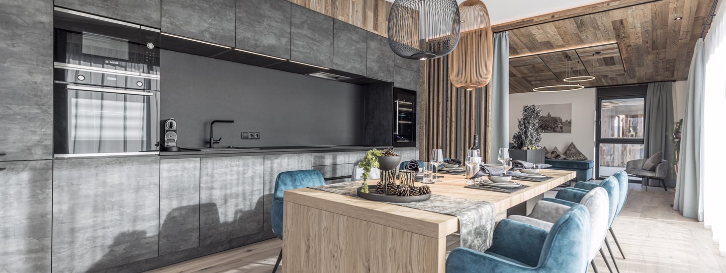 Großzügiger Essbereich im Penthouse mit langem Holztisch, blauen Polsterstühlen und moderner offener Küchenzeile.