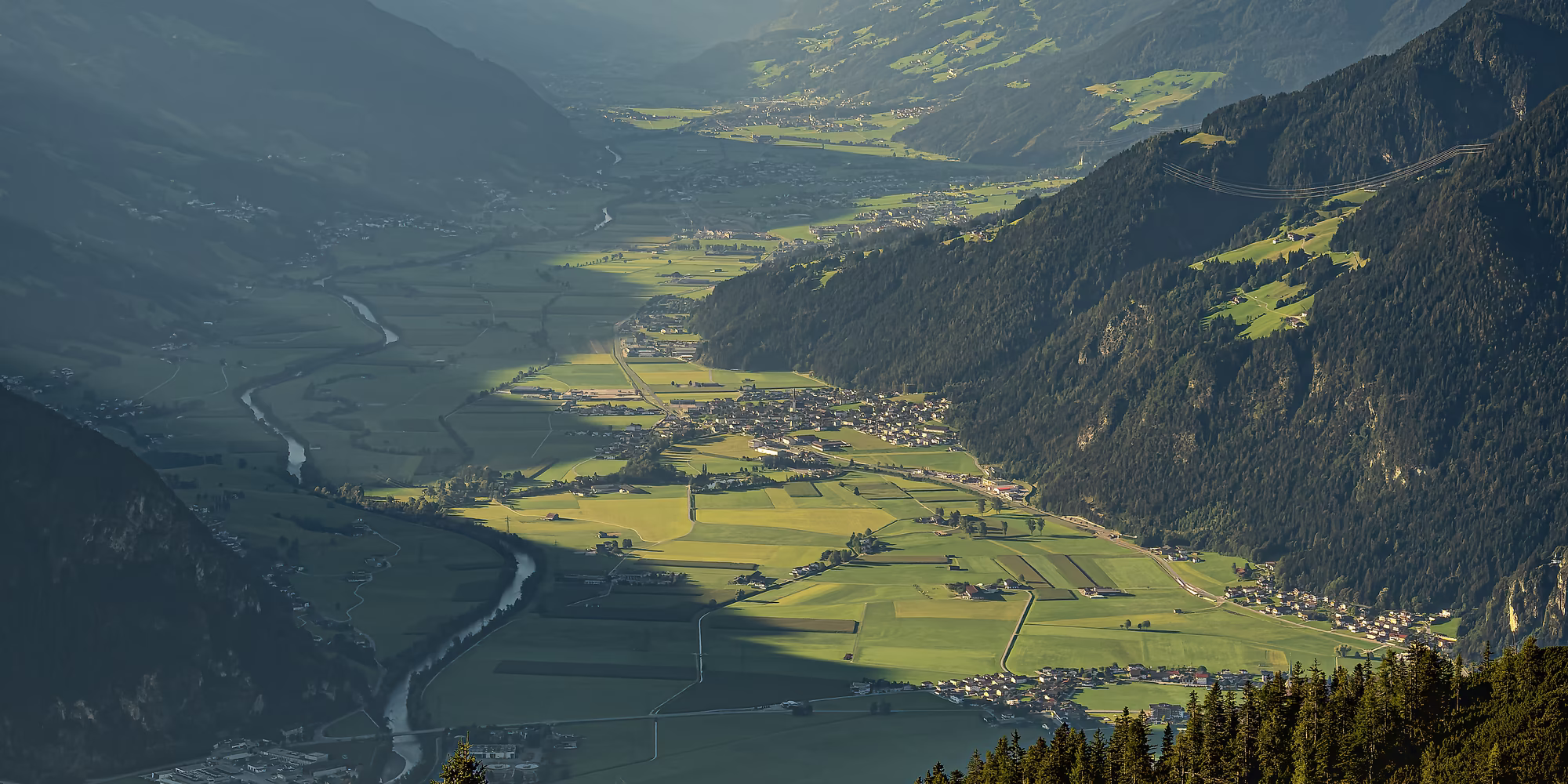 Weiter Ausblick über grüne Felder, Dörfer und den Ziller durch die Erste Ferienregion bis zu den Gipfeln des Zillertals.