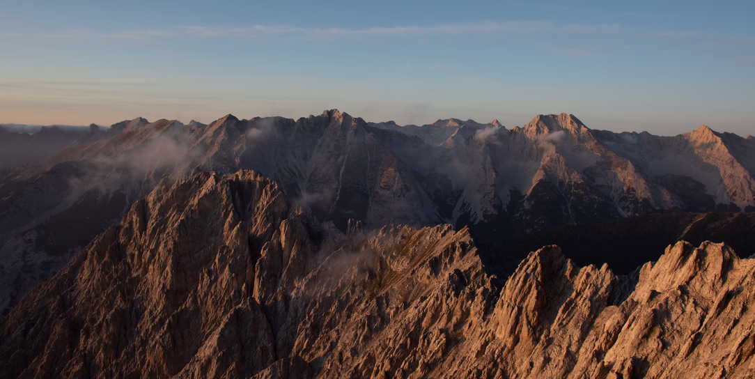 Weitläufiges Panorama der schroffen Gipfel am Hafelekar bei Innsbruck im warmen Licht mit einzelnen Wolken zwischen den Bergen.