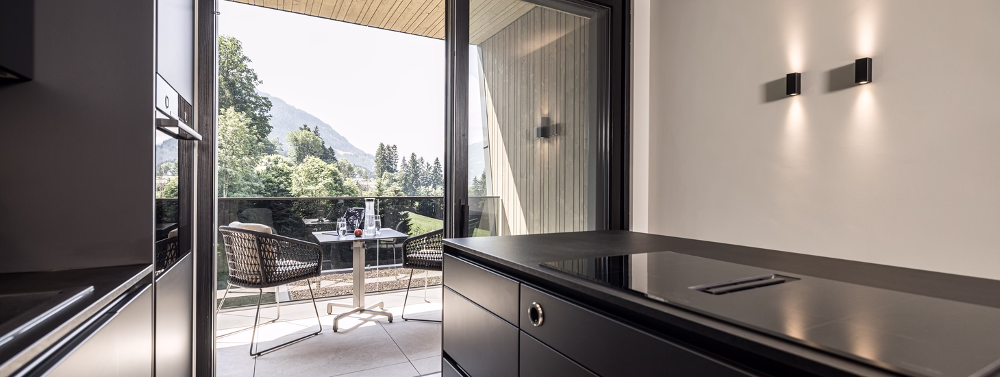 Die moderne schwarze Küche der Panorama Nature Lodge öffnet sich direkt zum möblierten Balkon mit Blick ins Grüne.