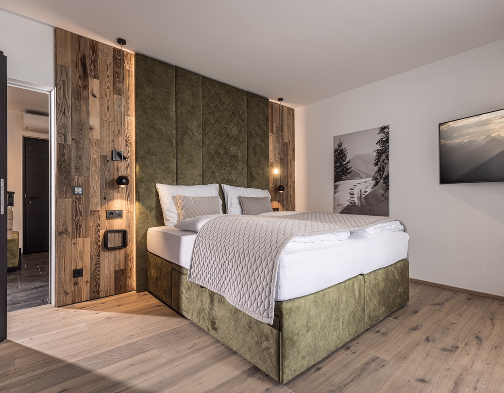 Modernes Doppelzimmer mit grünem Kopfteil, rustikaler Holzeinfassung, Wintermotiv und großem Fernseher.