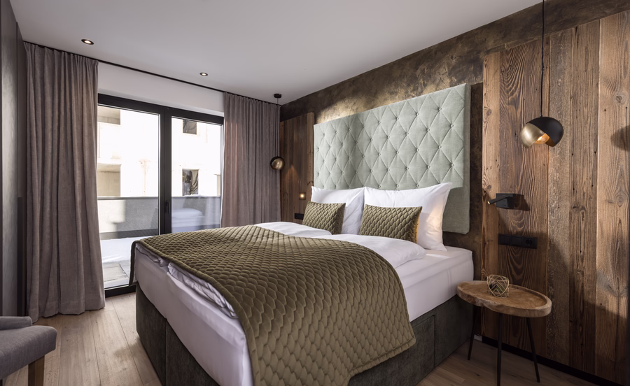 Modernes Schlafzimmer mit Doppelbett in Grüntönen, warmen Holzwänden und direktem Zugang zum Balkon.