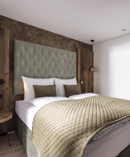 Gemütliches Schlafzimmer mit großem Doppelbett, grünem Polsterkopfteil, passenden Textilien und rustikalen Holzelementen.
