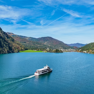 Ein Ausflugsschiff fährt über den Achensee, umgeben von bewaldeten Bergen und einer sonnigen Uferlandschaft.