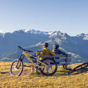 Zwei Mountainbiker sitzen mit ihren Fahrrädern auf einer Bank und blicken auf die Bergwelt rund um Gerlos.