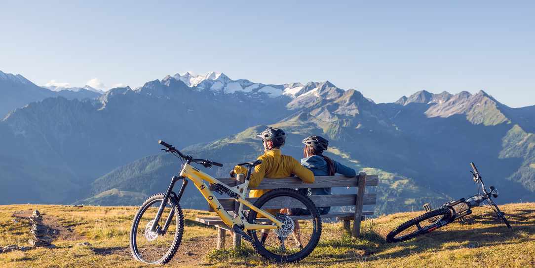 Zwei Mountainbiker sitzen mit ihren Fahrrädern auf einer Bank und blicken auf die Bergwelt rund um Gerlos.