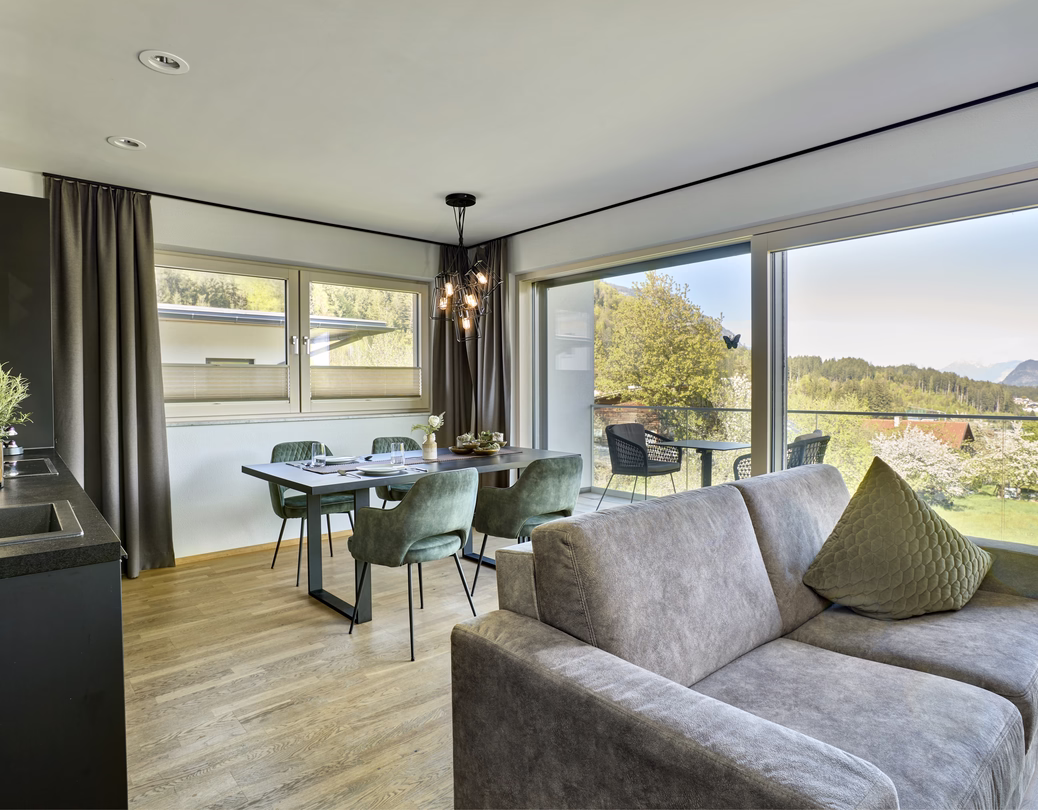 Moderner Essplatz mit grünen Polsterstühlen, angrenzender Küche und bodentiefen Fenstern zum Balkon mit Panoramablick.