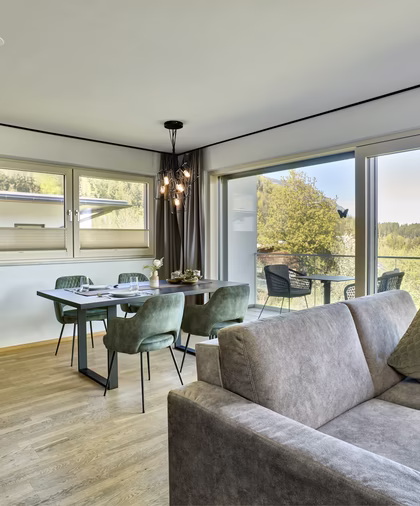 Moderner Essplatz mit grünen Polsterstühlen, angrenzender Küche und bodentiefen Fenstern zum Balkon mit Panoramablick.