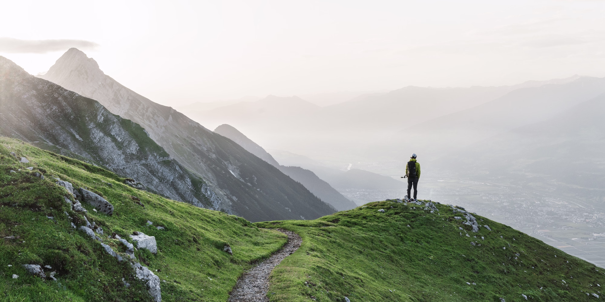 Wanderer steht auf einem grünen Bergrücken am Goetheweg und blickt über das Inntal und die umliegenden Berge.