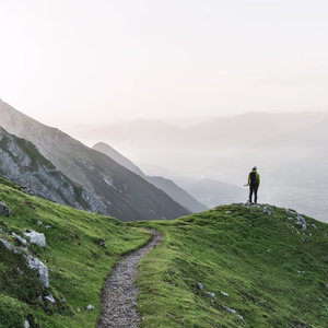 Wanderer steht auf einem grünen Bergrücken am Goetheweg und blickt über das Inntal und die umliegenden Berge.