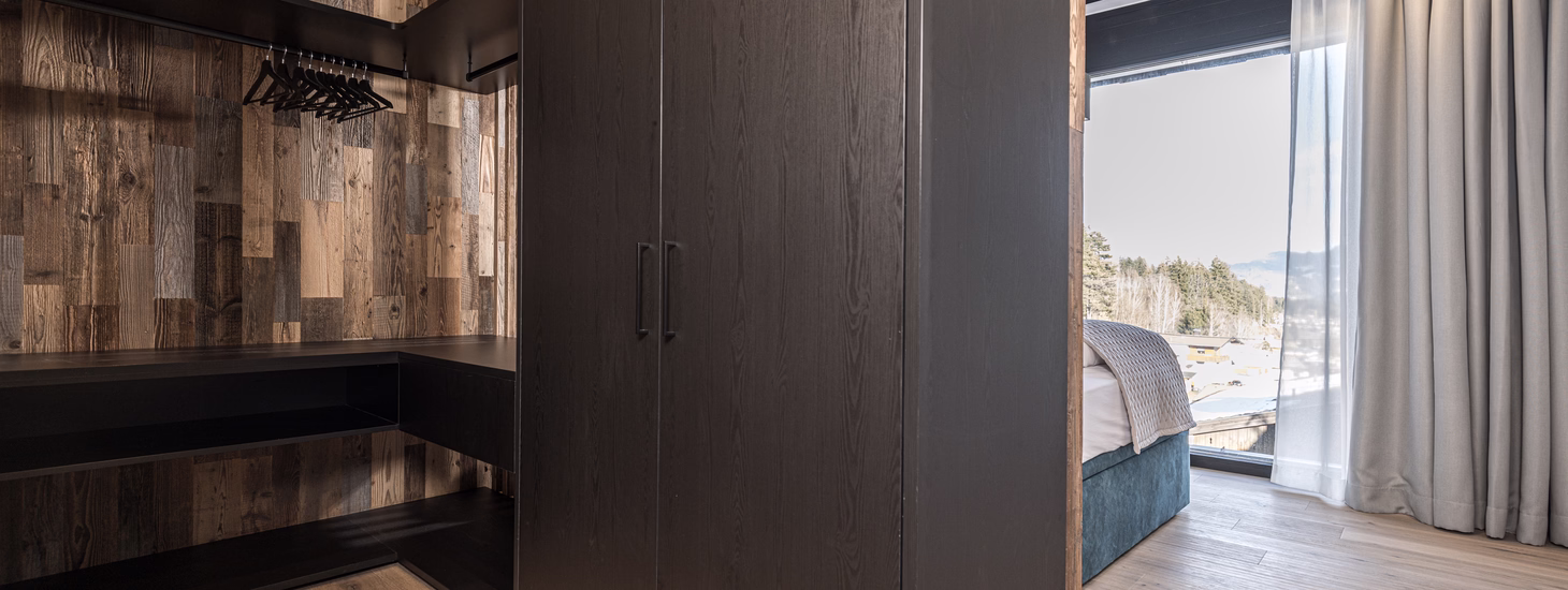 Geräumiger offener Kleiderschrank mit dunklen Einbauten und rustikaler Holzwand direkt neben dem hellen Schlafzimmer.
